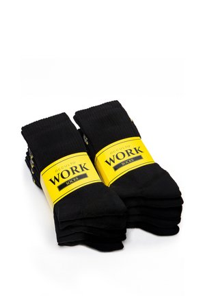Person mit Smartwatch zieht schwarzen Socken mit grauer Spitze und gelbem Streifen an, während sie auf weißem Boden sitzt.