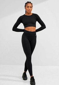 Black ribbed crop top with long sleeves paired with high-waisted black leggings. Fabric has a textured finish; both items feature a fitted design.
