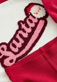 Czerwony sweter z teksturowanym wzorem "Świętego Mikołaja" w różowym i bordowym włóczce. Żebrowane czerwone akcenty na dole. Miękka tkanina na białym tle.