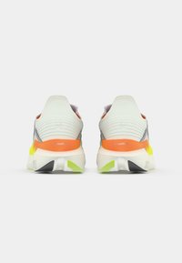 Baskets de course en blanc, gris et orange avec un dessus en maille texturée. Dotées d'une semelle rembourrée avec des accents verts et noirs pour une meilleure traction.