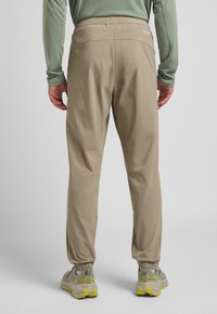 Pantaloni beige leggeri con vita elastica e orli affusolati. La trama è liscia, con dettagli minimi e un design funzionale.