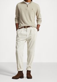 Beige zip-neck tröja, krämfärgade manchesterbyxor, brun läderrem, och mörkbruna mockastövlar. Enkel, skräddarsydd design med framfållar.