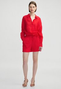 Conjunto de camiseta y pantalones cortos de lino rojo con un acabado texturizado, corte relajado, frente abotonado y un cinturón atado en la cintura.