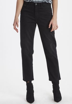 Jeans de mezclilla negra con un corte recto, que cuentan con cinco bolsillos y un cierre de botón. Llevados con botas negras de tobillo. Textura suave.
