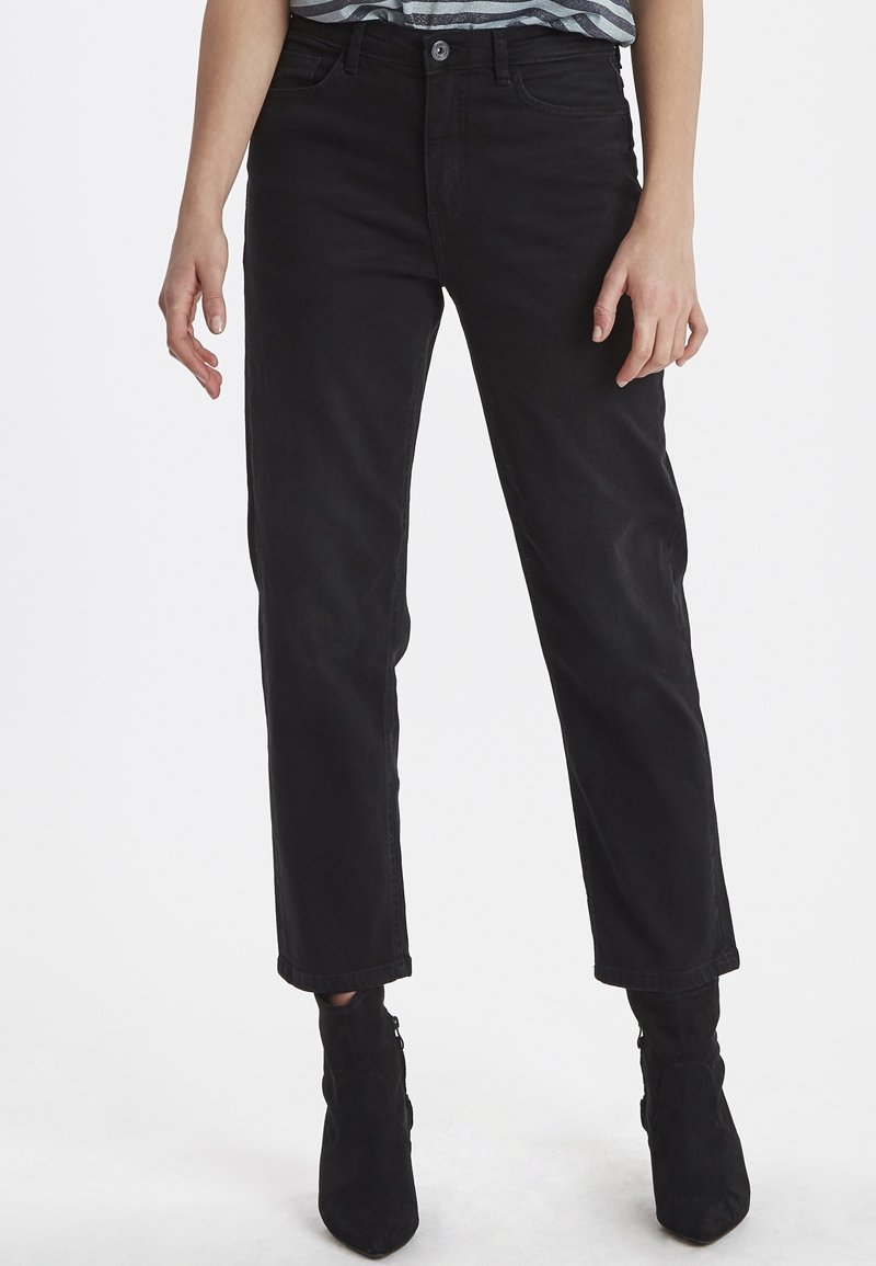 Jeans de mezclilla negra con un corte recto, que cuentan con cinco bolsillos y un cierre de botón. Llevados con botas negras de tobillo. Textura suave.