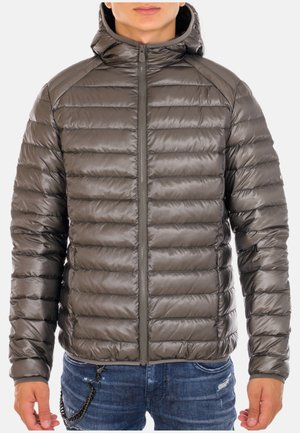 Man draagt een donkergrijze pufferjas met ritssluiting en capuchon, gecombineerd met versleten blauwe spijkerbroek, tegen een witte achtergrond.