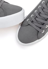 Gray canvas sneakers with white rubber soles and eyelets. Features flat gray laces and a textured finish on the upper material.