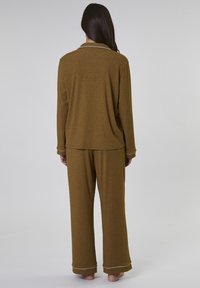 Olivgrön pyjamasset bestående av en långärmad topp och vida byxor. Toppen har en enkel krage; ärmsluten och byxans fåll har vit kant.