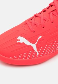 Scarpa sportiva rossa con tomaia texturizzata, logo bianco e design con lacci. Presenta una suola con motivo per una migliore aderenza.