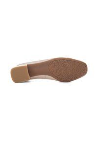 Chaussure beige clair avec une tige lisse et une semelle en caoutchouc texturée. Le talon est de forme bloc, offrant stabilité et adhérence. Des motifs notables sur la semelle.