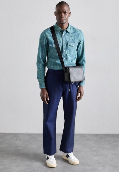 Camicia a maniche lunghe a righe turchesi, pantaloni blu navy e sneakers bianche. Una borsa a tracolla nera completa il look, con hardware semplice.