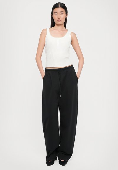 White ribbed tank top with a scoop neckline paired with black wide-leg sweatpants featuring an elastic waistband and side pockets.
