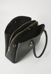 Black leather tote bag featuring two large compartments, a zip closure, and gold hardware accents. The exterior has a smooth texture.