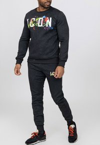 Ensemble sweat-shirt et joggers noirs avec un design graphique coloré "ICON" sur le devant. Comprend des poignets et une taille côtelés, texture douce.