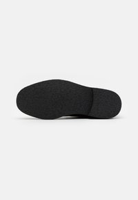 Suela de zapato de goma negra con superficie texturizada, punta redondeada y sección de tacón curvada. Sin marcas visibles ni elementos decorativos.