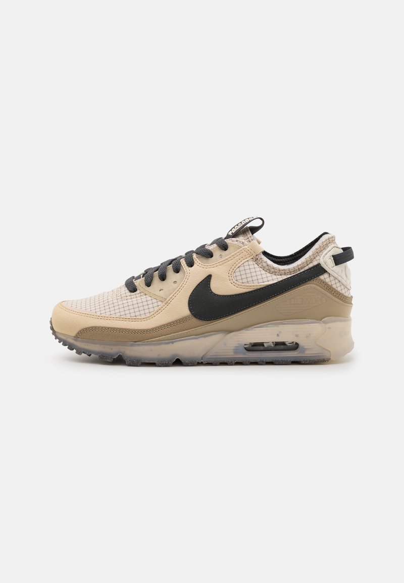 Beige Sportschuh mit schwarzen Akzenten, der ein Obermaterial aus Mesh, strukturierte Überzüge und eine sichtbare Luftpolsterung in der Sohle aufweist. Graue Schnürsenkel.