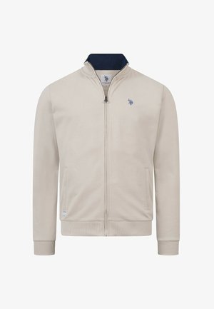 Beige Reißverschlussjacke mit gerippten Bündchen und Kragen, marineblauem Innenkragen, zwei Seitentaschen und kleinem, blau besticktem Logo auf der linken Brust.