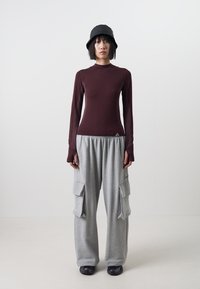 Vinröd långärmad topp med figurnära design, kombinerad med lösa grå cargobyxor med sidofickor. Svart bucket hat fulländar looken.