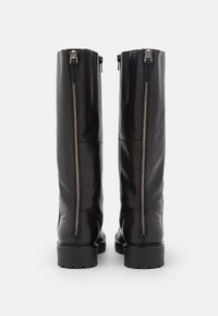Botas de cuero negras hasta la rodilla con una textura suave, que cuentan con dos cremalleras centrales y una suela de goma resistente.