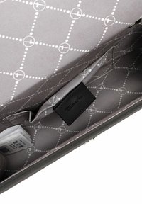 Interior de bolso de tela gris que presenta un patrón geométrico con círculos y líneas blancas, incluye una etiqueta negra y compartimentos visibles.