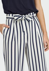 Pantalones de tiro alto a rayas en blanco con franjas marino, con un cinturón con lazo, pliegues y bolsillos laterales. Textura de tela suave.