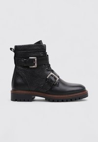 Bottines en cuir noir avec une finition texturée, deux boucles et une semelle en caoutchouc avec des rainures de traction. Design classique à bout rond.