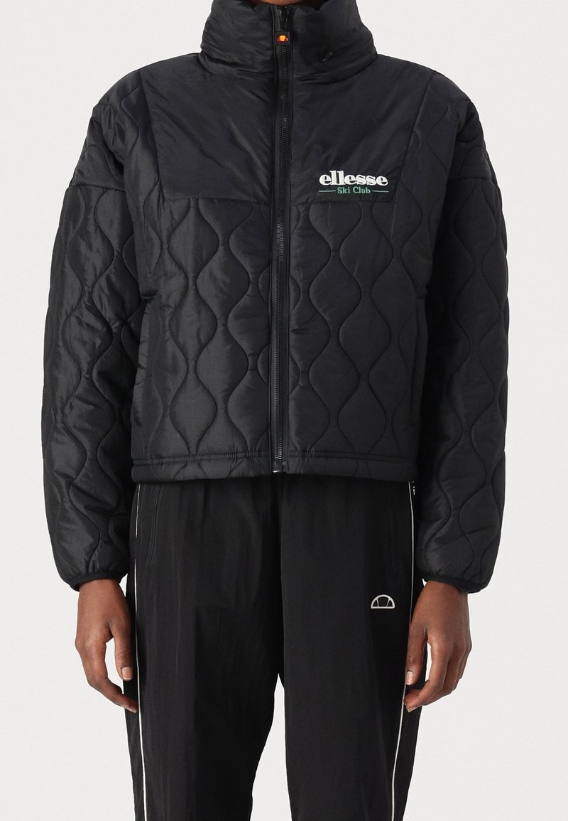 Czarna pikowana kurtka z wysokim kołnierzem, z zamkiem błyskawicznym z przodu i logo. Teksturowany wzór i krótki fason, połączona z czarnymi spodniami.
