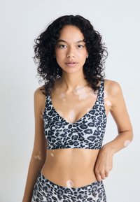 Bralette i leopardmønster med v-halsdesign, mykt stoff og brede stropper. Fargesammensetningen inkluderer nyanser av grått og svart.