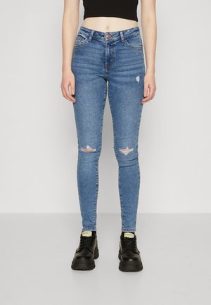 Jeans skinny bleus avec détails déchirés aux genoux, fabriqués en denim, design taille haute, associés à des chaussures noires à semelles épaisses.