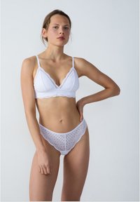 Bralette en dentelle blanche et hipster assorti. Présente des bords festonnés, un motif géométrique délicat et des bretelles fines. Texture lisse.