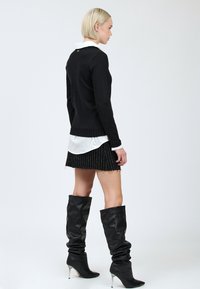 Maglione nero a maglia con orlo a coste, indossato su una camicia bianca con colletto e una minigonna nera a righe verticali. Stivali alti neri, morbidi e con tacco.
