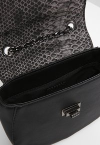 Černá kabelka s texturovaným klopovým dílem se vzorem hadí kůže. Interiér je podšívkovaný měkkým materiálem. Stříbrný řetízkový detail a uzávěr na sponu.