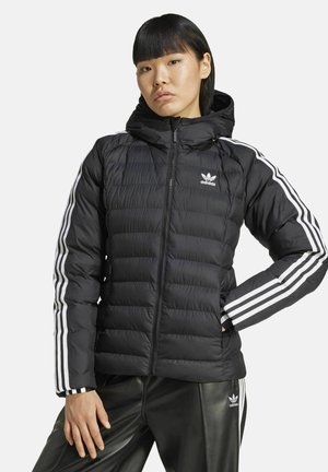 Zwarte pufferjack met een ritssluiting aan de voorkant, capuchon en wit Adidas-logo. Heeft verticale geplaatste stiksels en drie witte strepen op de mouwen.