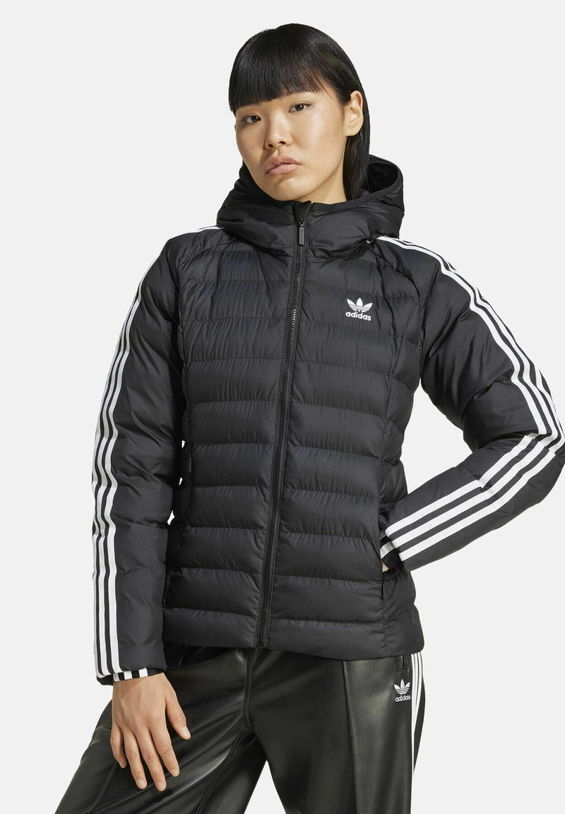 Giubbotto imbottito nero con zip frontale, cappuccio e logo Adidas bianco. Presenta sezioni trapuntate verticali e tre strisce bianche sulle maniche.
