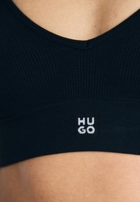 Zwarte geribbelde sportbh met een V-hals en een merktag met de tekst "HUGO" in het wit. Glad textuur en aansluitend ontwerp voor comfort.