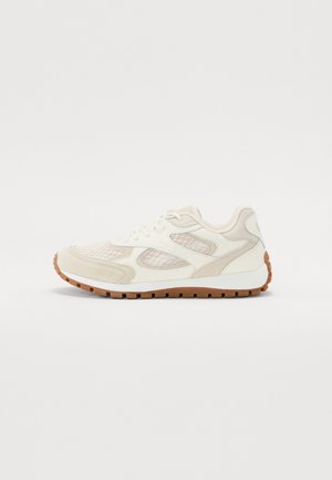 Krémová teniska s síťovými panely, semišovými detaily, bílou mezipodešví a hnědou gumovou podešví s vzorem, zobrazená z boku.