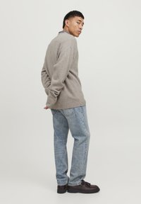 Maglione beige a maglia con polsini e orlo a costine, abbinato a jeans diritti azzurri e scarpe marroni scure, visto di lato.