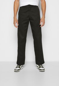 Dark green straight-leg pants made from a sturdy fabric, featuring belt loops and side pockets, paired with black and white sneakers.