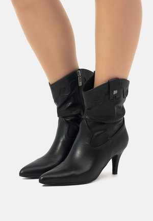 Botas de tobillo de cuero negro con un diseño arrugado, punta afilada y un tacón de 3 pulgadas; incluyen un cierre lateral y costuras decorativas.