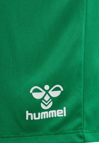 Groen textiel met wit Hummel sportkledinglogo met een gestileerde bij en merknaam bij een naad.