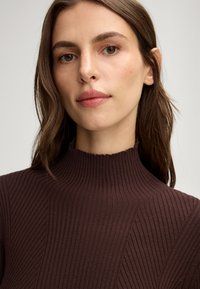 Brauner gerippter Pullover mit einem hohen Kragen, der strukturierte vertikale Linien und eine taillierte Silhouette aufweist. Weicher Stoff mit leichtem Stretch.