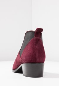 Burgundy suede ankle boot with a low black heel, elastic side panels, and a tab at the back for easy fitting. Smooth texture.