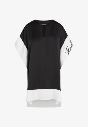 Zwart-witte tuniekjurk met een V-hals, wijde mouwen en "Karl" geborduurd op de linkermouw.