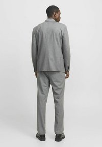 Pilkas kostiumas, pagamintas iš tekstūruoto audinio, struktūrizuotas švarkas su viena ventiliacija ir derančios kelnes tiesiu kirpimu bei juodais batais.