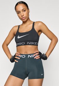 Czarny stanik sportowy z białym logo Nike i szarymi szortami z wysokim stanem, które mają biały pasek "PRO NIKE". Czarne rękawiczki bez palców.