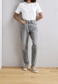 White cotton t-shirt, high-waisted light gray jeans with five pockets, and beige sneakers with laces. Standing on a wooden floor.