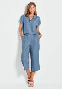 Denim-Overall in Hellblau, mit kurzen Ärmeln, Kragen, elastischem Bund und weit geschnittenen, kurzen Beinen. Getragen mit mehrfarbigen Plateausandalen.