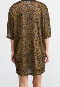 Knälång, löst sittande klänning i ett genomskinligt tyg med leopardmönster i guldbrunt och svart. Korta ärmar, rund halsringning och rak skärning.