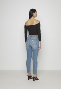Top preto sem mangas, combinado com jeans de cintura alta azul claro, apresentando um emblema na parte de trás e detalhes desgastados. Saltos pretos.