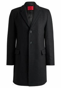 Cappotto in lana nera con revers a punta, tre bottoni, due tasche frontali e foderatura liscia. Linee pulite e silhouette sagomata.